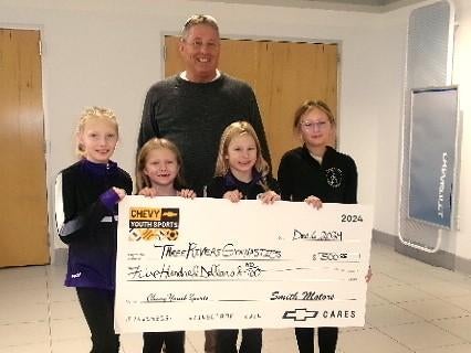Four girls holding a large check in front of a man